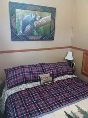 A bed with a plaid bedspread and a pillow labeled 'BEAR.'