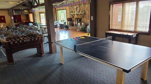 A ping pong table in a room with a foosball table and a fireplace.