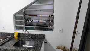Una cocina con encimera de granito, pileta de acero inoxidable, ventana con rejas y una planta en maceta.
