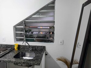 Uma cozinha com bancada de granito, pia de aço inoxidável, janela com grades metálicas e uma planta em vaso.