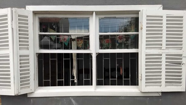 Una ventana con contraventanas blancas, una reja de metal y un picaporte visible.