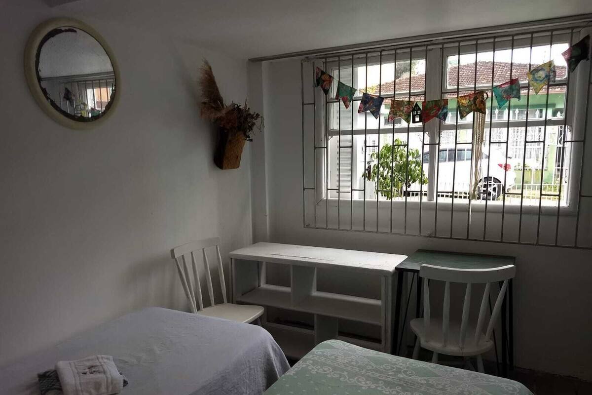 Una habitación con cama, escritorio, silla, espejo y ventana con vistas al exterior.