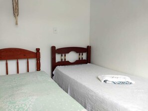 Quarto com duas camas de solteiro, uma com colcha estampada e outra com colcha lisa.