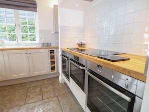 A modern kitchen with white cabinets, a wooden countertop, a built-in oven, and a window with a view of greenery. - Island Cottage Rod Eyot (Henley-on-Thames)
