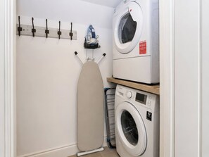 A laundry room with a washing machine, an ironing board, and a drying rack. - Island Cottage Rod Eyot (Henley-on-Thames)