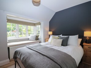 A bedroom with a large bed, a window seat, and a view of greenery outside. - Island Cottage Rod Eyot (Henley-on-Thames)