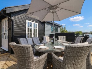 A dining area with wicker chairs and a glass table, an umbrella, and a view of a river. - Island Cottage Rod Eyot (Henley-on-Thames)
