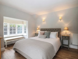 A bedroom with a large bed, two bedside tables, a bench, and a window with shutters. - Island Cottage Rod Eyot (Henley-on-Thames)