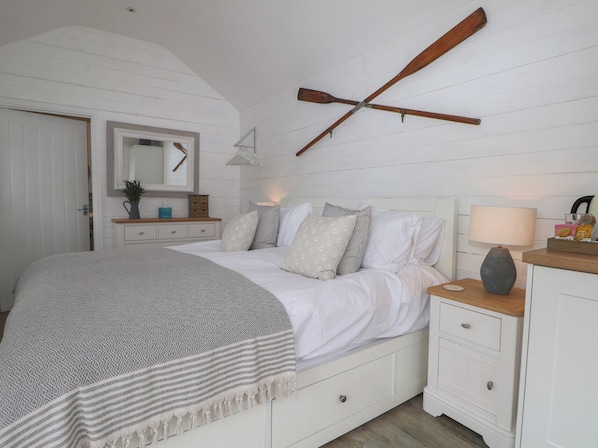 A bedroom with a bed, nightstand, dresser, and a wooden paddle on the wall. - Island Cottage Rod Eyot (Henley-on-Thames)