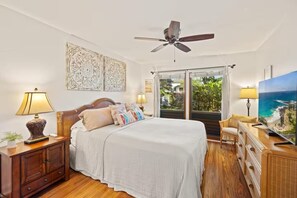 A bedroom with a bed, bedside tables, a ceiling fan, a large window with a view, and a television. - Walk to Poipu Beach, Grand Hyatt & Brennecke's/Poipu Kai Charming Condo (Koloa)