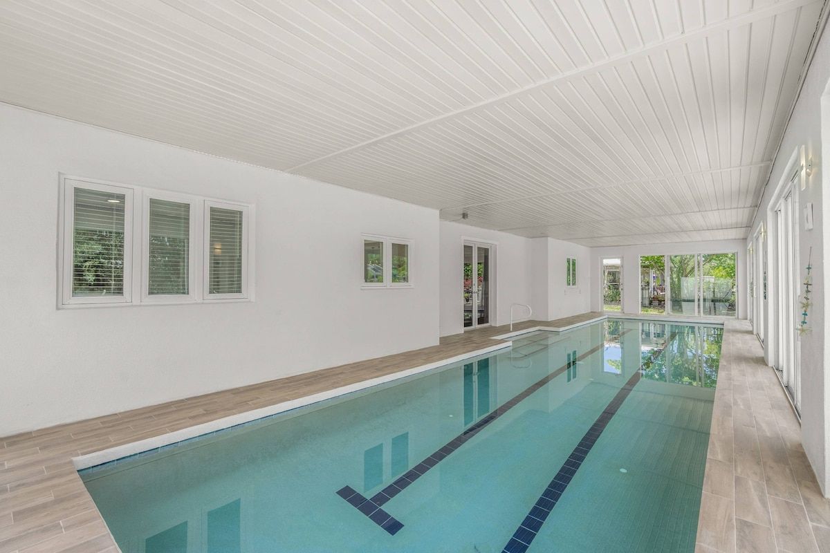 Una piscina interior larga con un muelle de madera y paredes blancas.