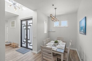 A dining area with a table set for four, a hanging light fixture, and a view through a door. - Siesta Swim House | Indoor Pool | 10 min to Beach (Sarasota)