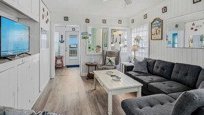 Una sala de estar con televisión, ventilador de techo, sofá y mesa de comedor.