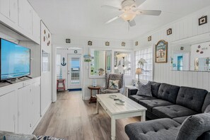 Ein Wohnzimmer mit Fernseher, Deckenventilator, Sofa und Esstisch.