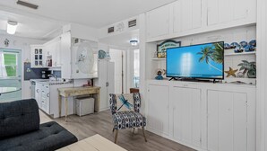 Un espacio habitable compacto con kitchenette, una zona de comedor, televisor montado en la pared y una silla con diseño decorativo.