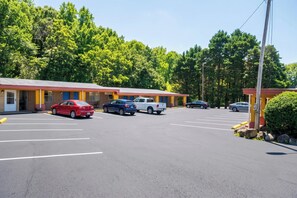 A motel with multiple parking spaces and a row of rooms with a red roof.