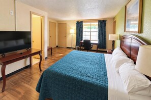 A hotel room with a bed, a desk with a television, a chair, and a window with curtains.