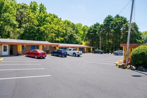 Um motel com várias vagas de estacionamento e uma fileira de quartos com fachada de tijolos e detalhes em amarelo.