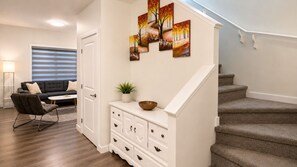 A modern living room with a sofa, coffee table, and a staircase. - Heartland Stays - Brand New 3 Bed Room Cozy Home with AC, Garage, BBQ (Cochrane)