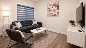 A modern living room with a sofa, coffee table, and TV. - Heartland Stays - Brand New 3 Bed Room Cozy Home with AC, Garage, BBQ (Cochrane)