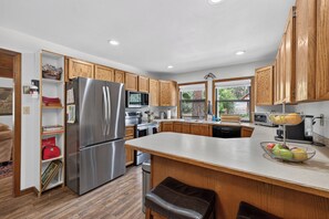 A modern kitchen with wooden cabinets, stainless steel appliances, and a central island with seating. - Pilgrim Cove Basecamp: 4BR, 3BA mountain-view retreat in McCall. (McCall)