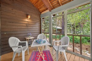 A covered porch with wooden walls, large windows, and white plastic chairs. - Pilgrim Cove Basecamp: 4BR, 3BA mountain-view retreat in McCall. (McCall)