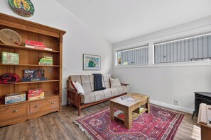 A cozy living room with a sofa, coffee table, and a wooden bookshelf filled with board games. - Pilgrim Cove Basecamp: 4BR, 3BA mountain-view retreat in McCall. (McCall)