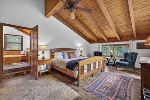 A bedroom with a wooden ceiling, a bed with a headboard, a desk, a chair, and a window. - Pilgrim Cove Basecamp: 4BR, 3BA mountain-view retreat in McCall. (McCall)
