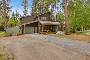 A two-story log cabin with a porch, a garage, and a large American flag. - Pilgrim Cove Basecamp: 4BR, 3BA mountain-view retreat in McCall. (McCall)