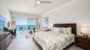 A bedroom with a bed, a desk, a chair, a lamp, a plant, a painting, and a view of the ocean. - One 1403B Studio: Beachfront Bliss Studio in Sandy Beach (Puerto Peñasco)
