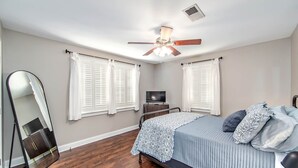 Quarto com cama, ventoinha no teto, televisão e um espelho grande.
