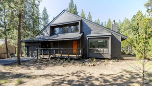 Een modern huis met twee verdiepingen en een ruim terras, omgeven door bomen.