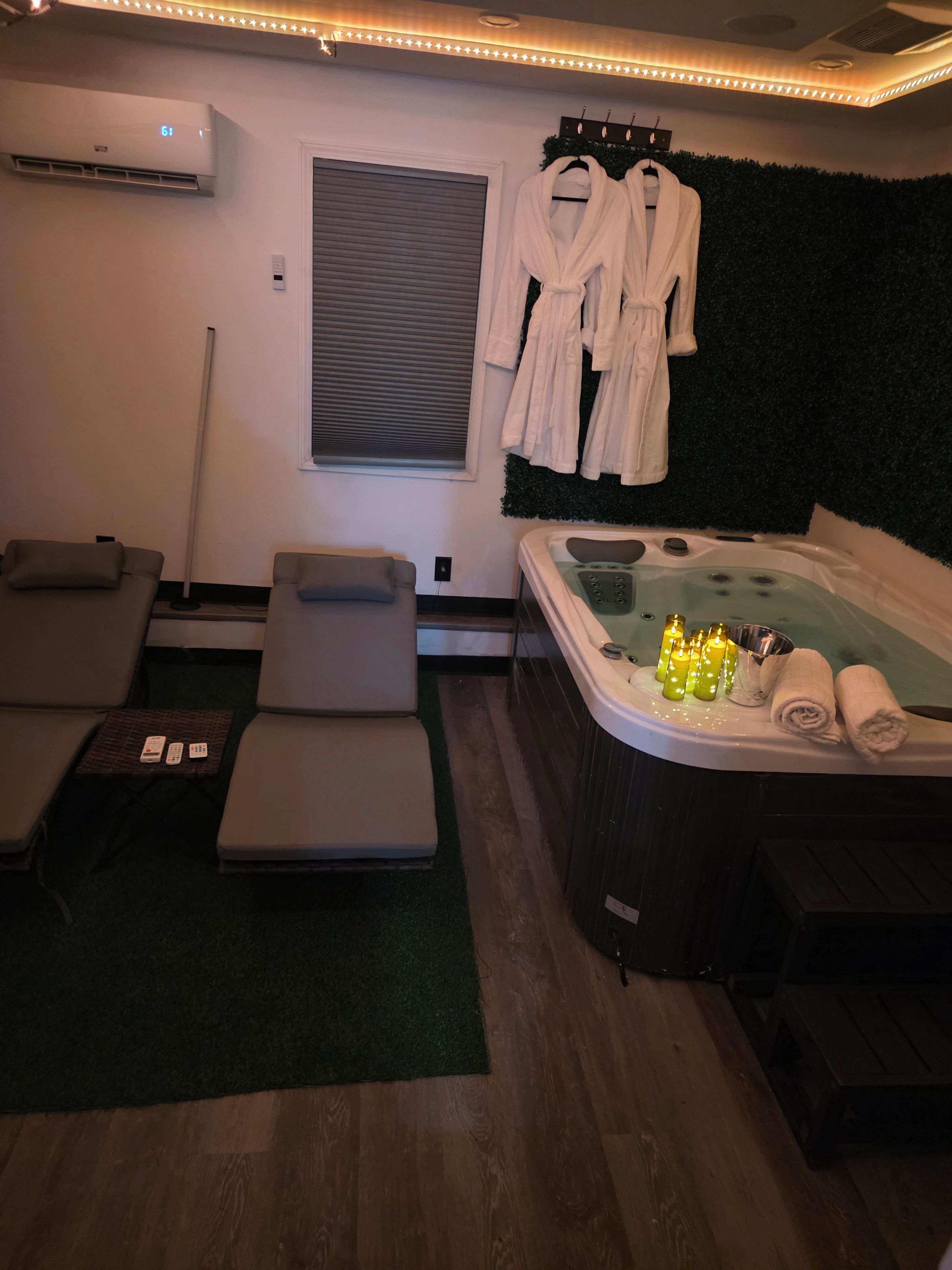 Ein Spa-Raum mit einer Massageliege, einer Whirlwanne mit Kerzen und Kleiderhaken mit Bademänteln.