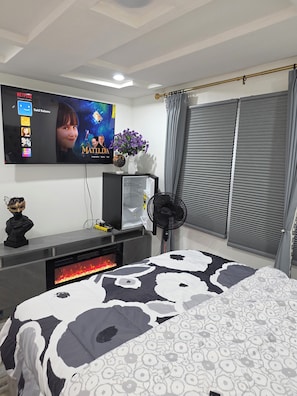 A bedroom with a bed, a TV mounted on the wall, a small table with a vase and a globe, and a fireplace.
