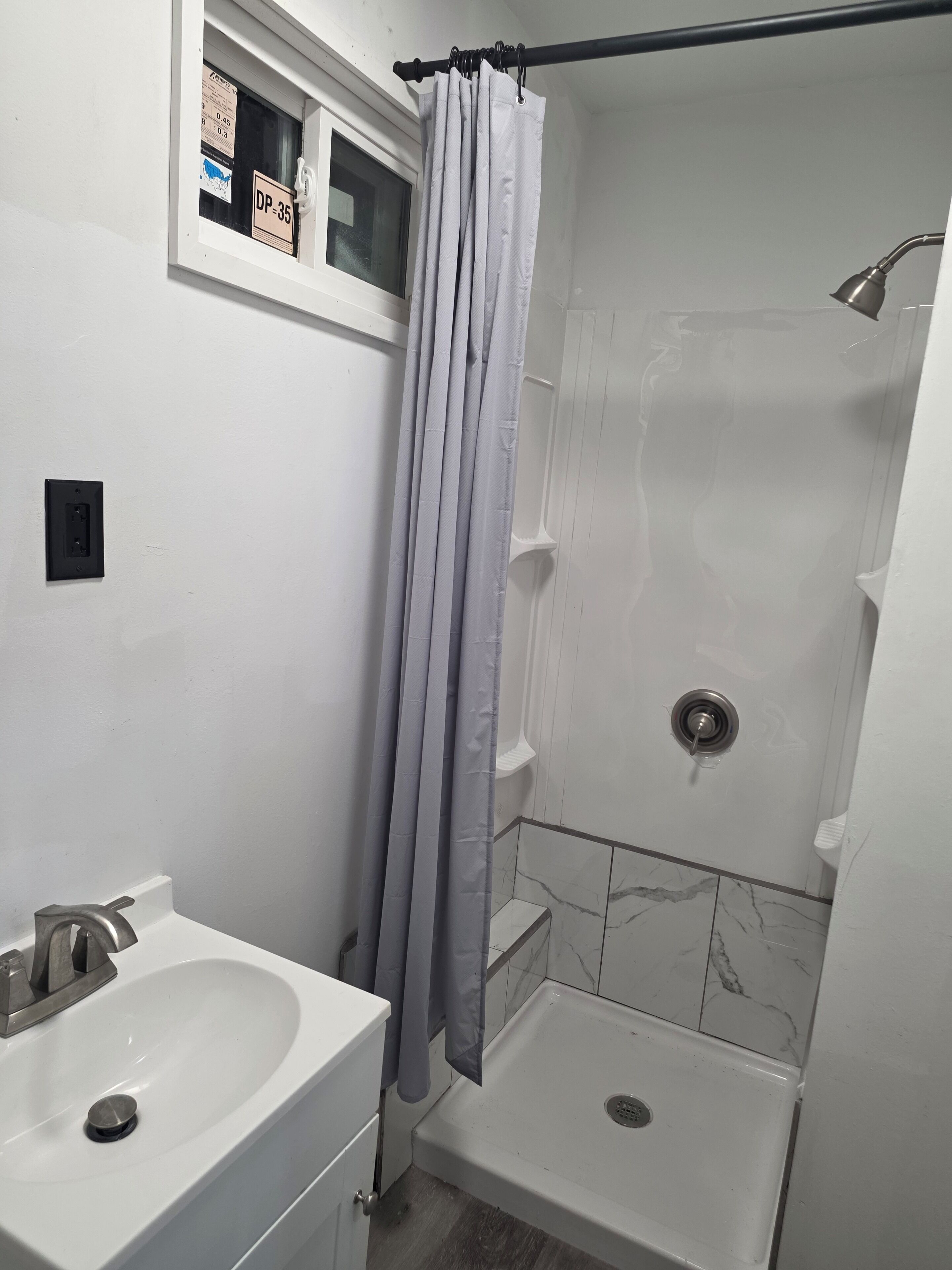 Une salle de bain avec une douche, un lavabo et une fenêtre sur laquelle est apposée une pancarte.