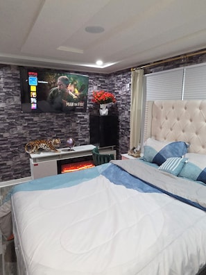 A bedroom with a bed, a TV mounted on the wall, a fireplace, and a decorative leopard statue. - Luxury 2BR Retreat ,Private Hot Tub, Starlink Wi-Fi ,Fireplace,Free Parking, (Syracuse)