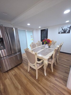 A dining area with a marble table, upholstered chairs, a stainless steel refrigerator, and a wall-mounted picture.