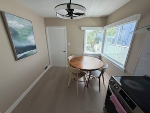 A dining area with a round table, chairs, a ceiling fan, a window with a view, and a kitchen area with a stove. - Newly renovated house in the heart of Vancouver! (Vancouver)