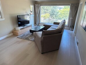 A modern living room with a flat-screen TV, a sofa, a coffee table, and large windows with curtains. - Newly renovated house in the heart of Vancouver! (Vancouver)