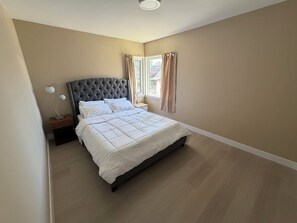 A bedroom with a large bed, a nightstand, a lamp, and a window with curtains. - Newly renovated house in the heart of Vancouver! (Vancouver)
