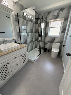 A modern bathroom with a glass shower enclosure, a white toilet, and a marble backsplash. - Newly renovated house in the heart of Vancouver! (Vancouver)