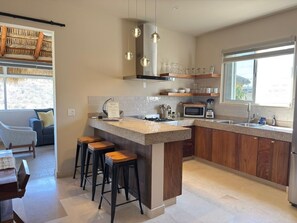 A modern kitchen with a central island, bar stools, a microwave, and a large window. - Private Home—Ocean View with Pool and Fire Pit (Perfect for Vacations) (BCS)