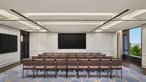 Un salón de conferencias con una pantalla grande, filas de sillas y una alfombra estampada.