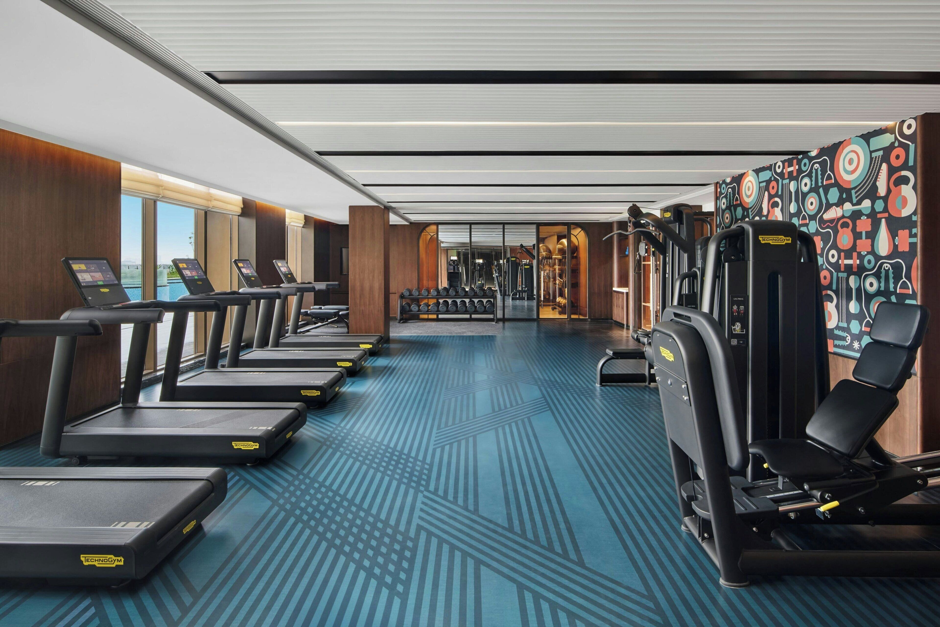 Une salle de sport équipée de tapis de course, d’appareils de musculation et dotée d’un sol à motifs.
