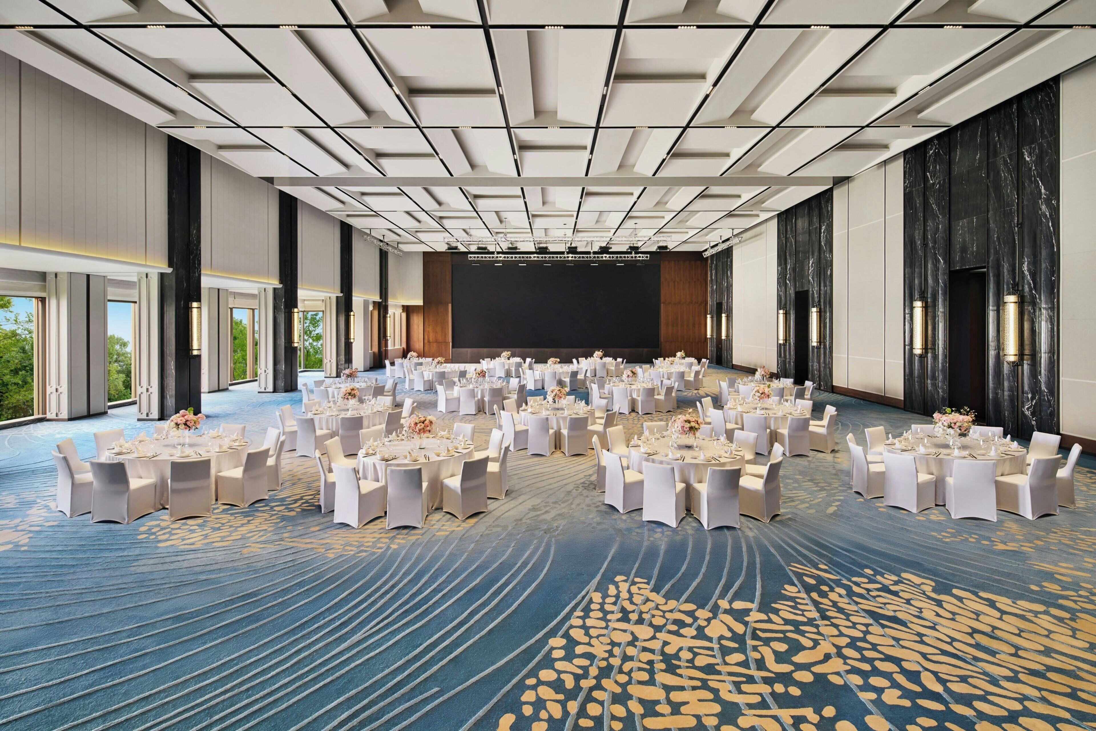 A large conference room with round tables, white chairs, and a stage at the front.