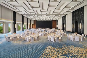 Un amplio salón de conferencias con mesas redondas, sillas blancas y un escenario al frente.