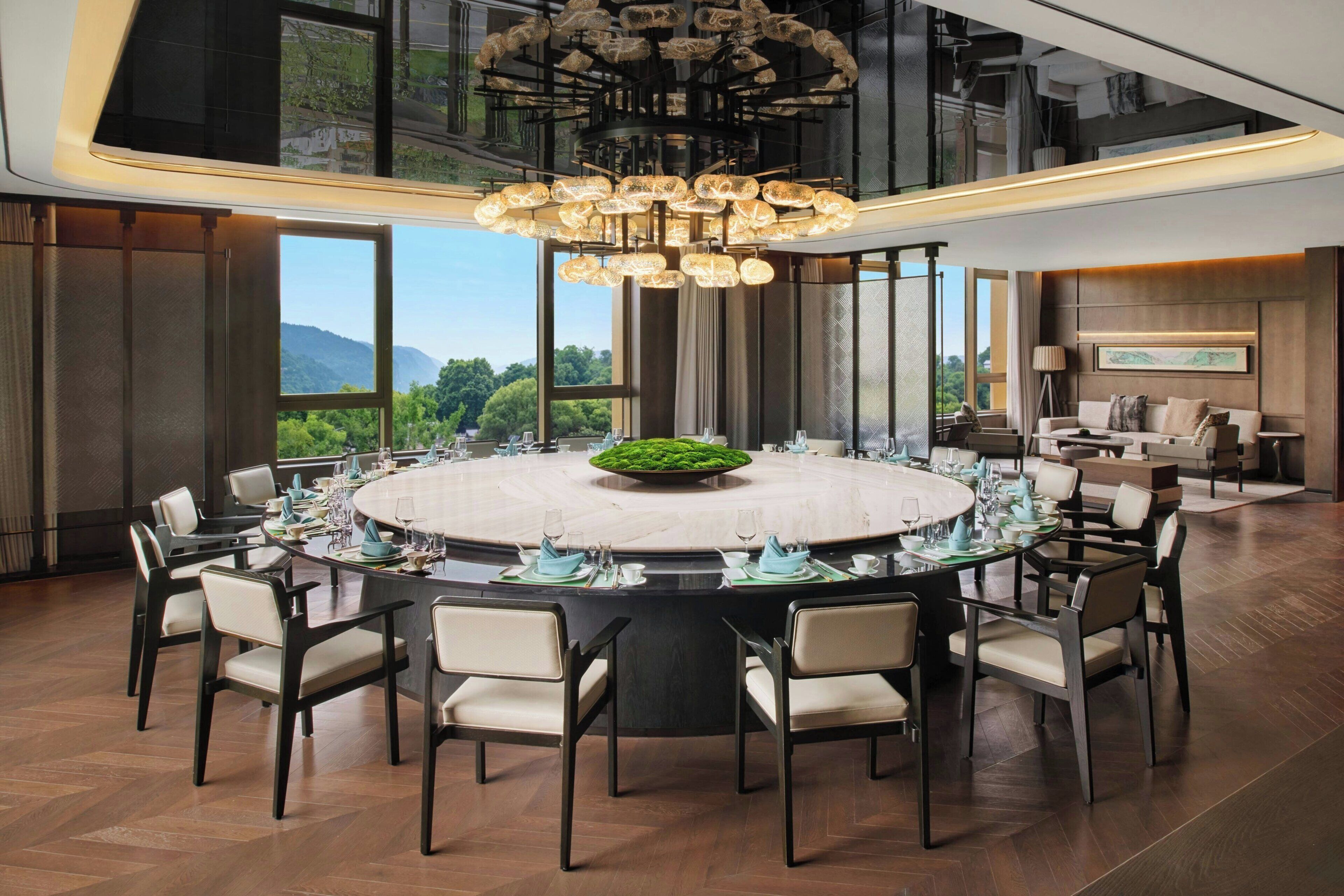 A spacious dining area with a round table set for a meal, surrounded by chairs, and a large chandelier above.
