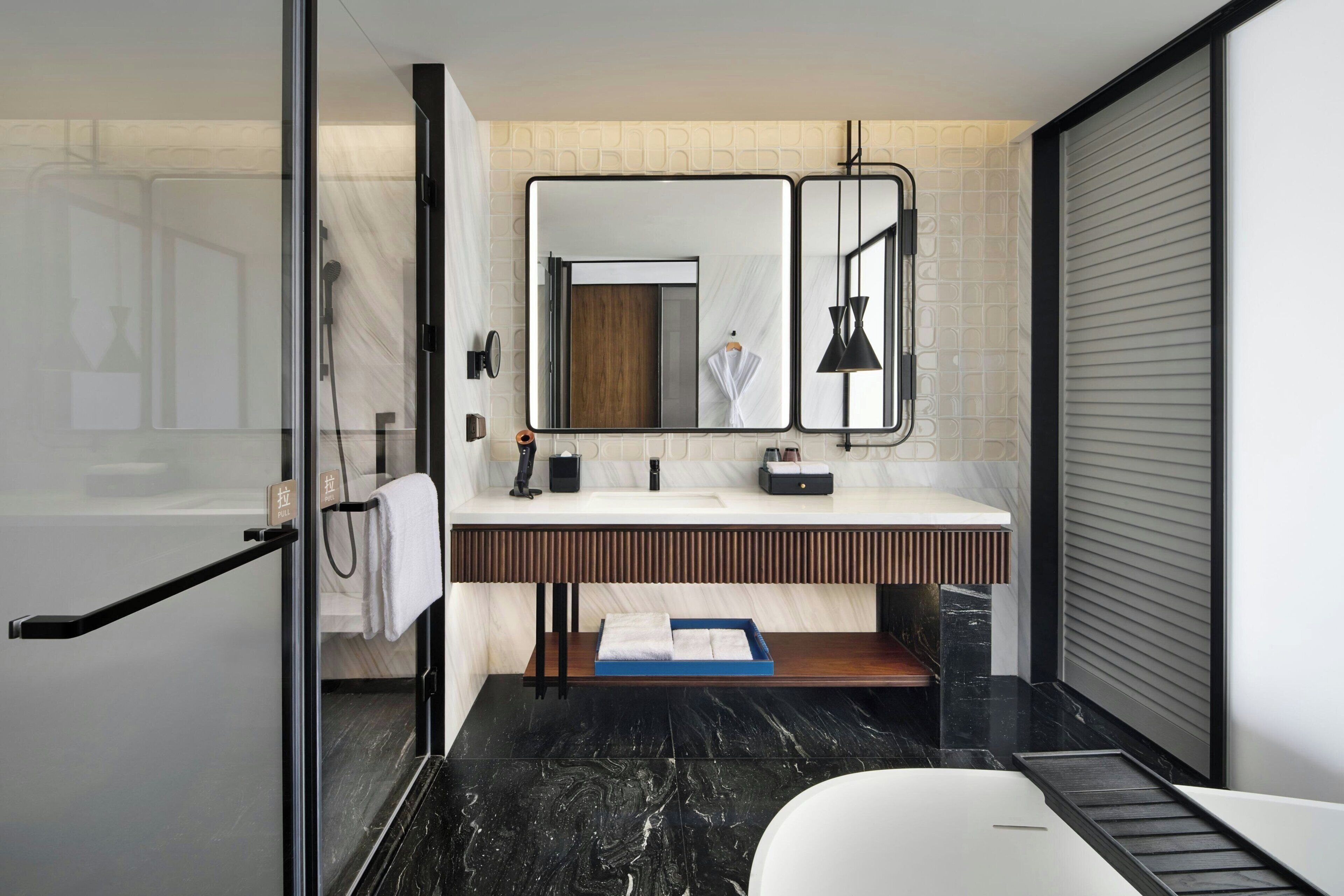 A modern bathroom with a glass shower enclosure, a white bathtub, a vanity with a mirror, and a towel rack.