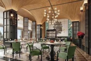 A spacious dining area with round tables and green upholstered chairs, a large chandelier, and a traditional Asian-style mural on the wall.