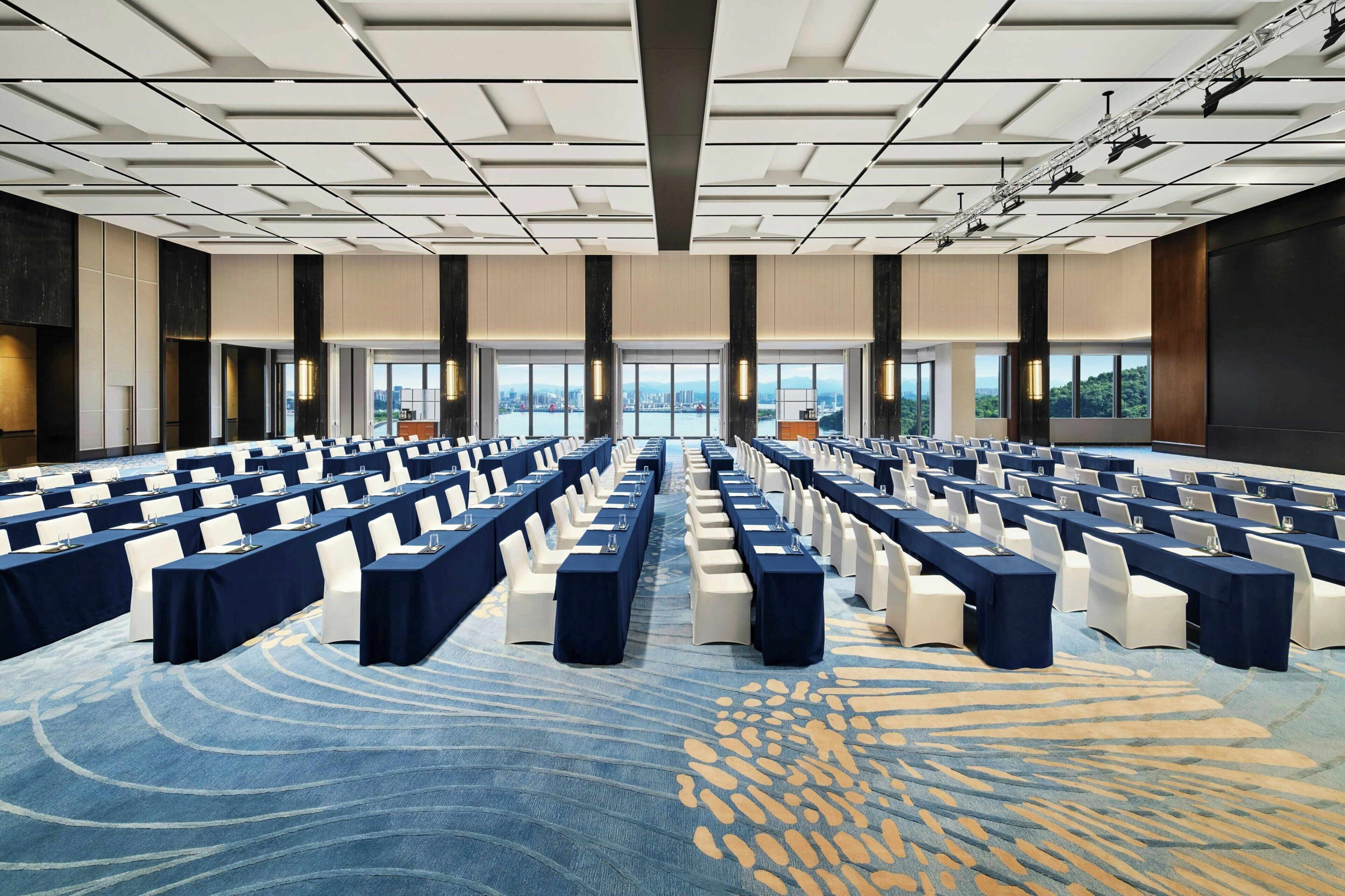 A conference room with rows of tables and chairs, large windows, and a modern ceiling design.